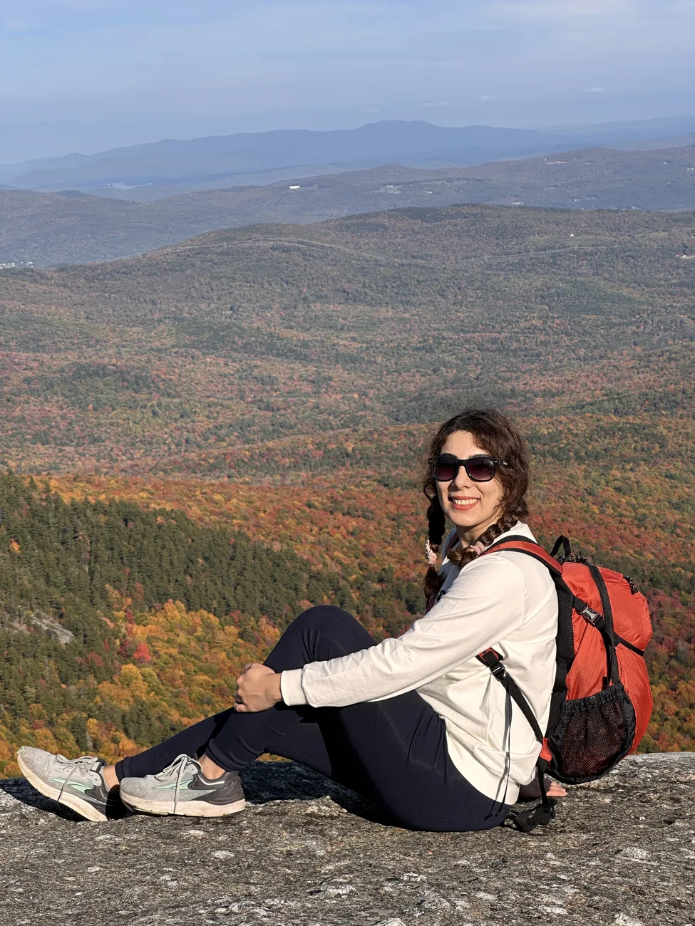 Maryam sitting on a rock above a valley of autumn forest.