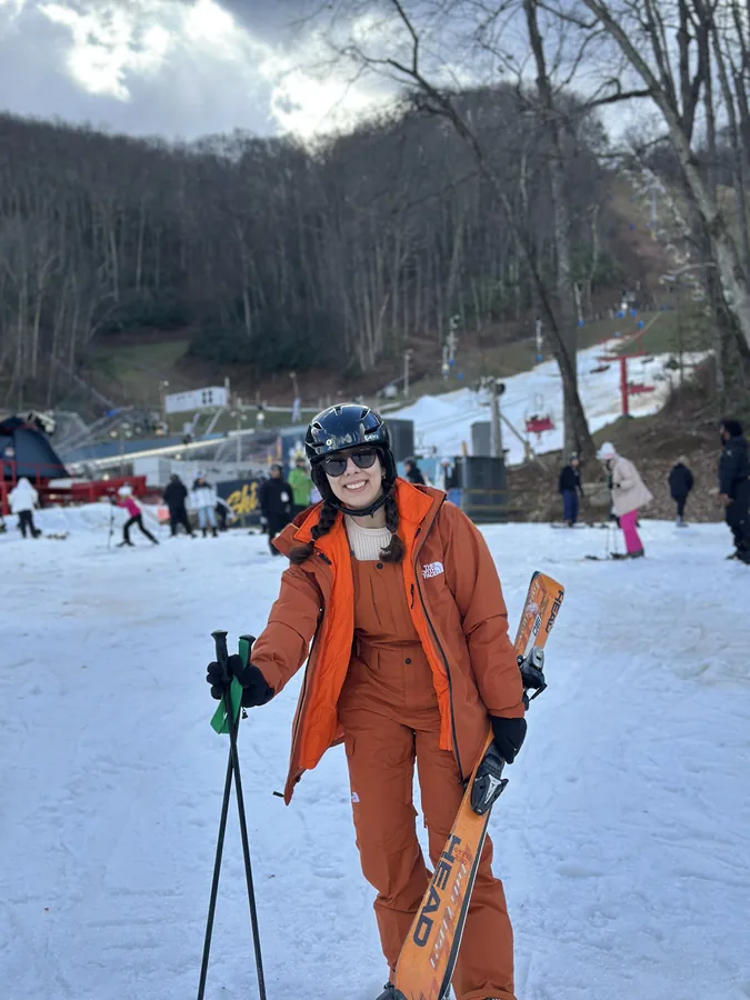 Maryam in orange ski gear at the bottom of a snowy run.